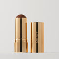 Master ||  A stick bronzer product by MERIT, with the cap off, showing the bronzing cream inside and MERIT on the cap. Shade Leo