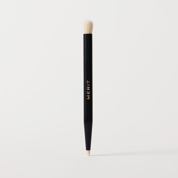 Master || A black cosmetic brush with a flat, dual-ended design, featuring the brand name 'MERIT' in gold lettering on the side.
