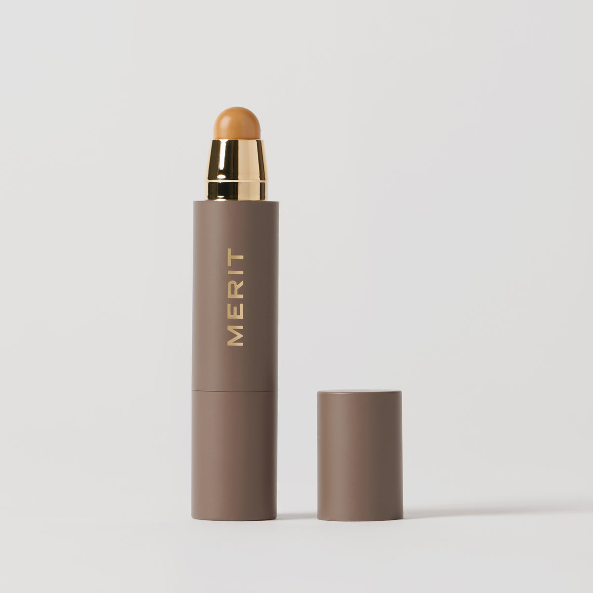 ** | listing A stick concealer product with the brand name 'MERIT' written on it, with the cap removed, showing the product in a shade of medium skin tone.