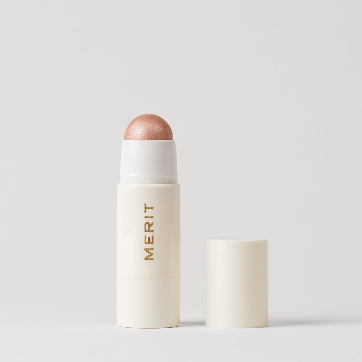 Master || A stick highlighter with the brand name MERIT written on it, with the product cap removed, revealing the highlighter balm 